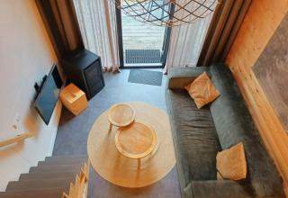 Living area of a tiny house seen from above, featuring a sofa, round tables, TV, and terrace doors.