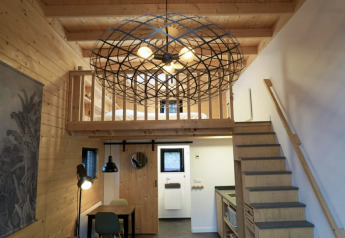 Interno di tiny house moderna con soppalco, scala in legno e grande lampadario geometrico sospeso.