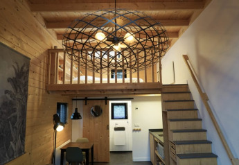 Intérieur de tiny house moderne avec mezzanine, escalier en bois et grand luminaire décoratif suspendu.
