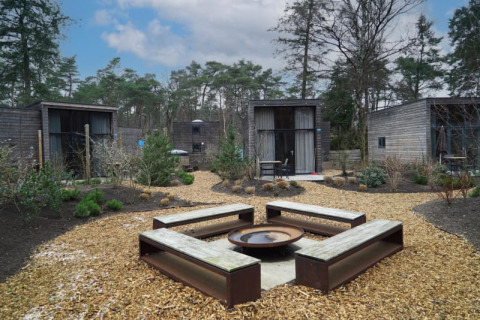 Zona exterior con bancos y fogata, rodeada de pequeñas casas minimalistas de madera en un entorno natural.