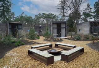 Zona exterior con bancos y fogata, rodeada de pequeñas casas minimalistas de madera en un entorno natural.