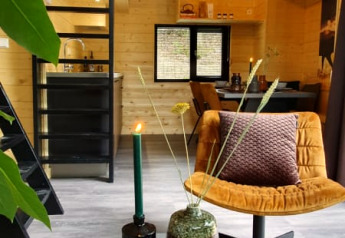 Gezellig tiny house interieur met houten wanden, zwarte ladder, gele stoel en rond, modern bijzettafeltje.