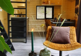 Interior moderno de tiny house con paredes de madera, escalera negra, sillón amarillo y mesa decorativa.