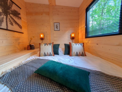 Acogedor dormitorio en una tiny house con paredes de madera, cojines decorativos, y ventana con vista al exterior verde.