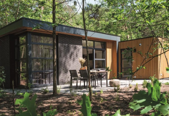 Modern lodge surrounded by forest, featuring large windows and an outdoor patio with dining furniture.