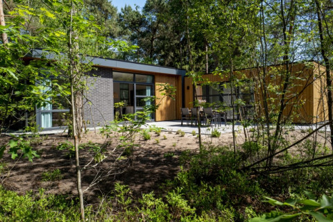 Lodge moderno rodeado de bosque, con grandes ventanales y terraza equipada con muebles de exterior
