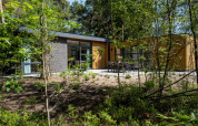 Modern lodge surrounded by forest, featuring large windows and a patio with outdoor furniture in nature