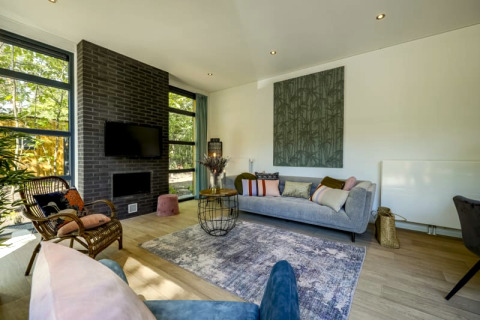 Salon moderne dans un lodge avec canapé gris, mur en briques noires, grandes fenêtres et parquet clair.