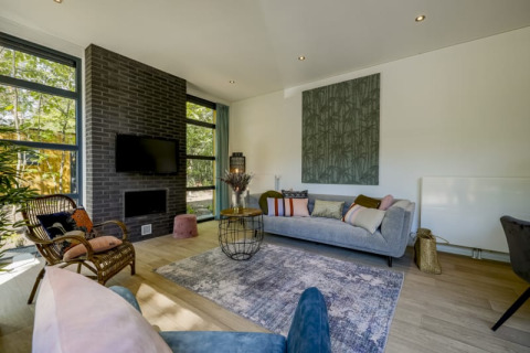 Salon moderne dans un lodge avec canapé gris, mur en briques noires, grandes fenêtres et parquet clair.