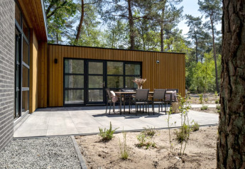 Moderne lodge met houten gevel, ruim betegeld terras en tuinset, omringd door bomen en natuur.