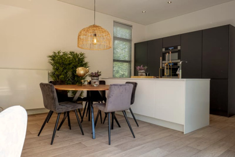 Cuisine moderne de lodge avec armoires noires, îlot blanc, table à manger ronde et chaises grises.