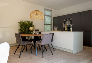 Modern lodge kitchen with black cabinets, white island, round dining table, grey chairs, and greenery.