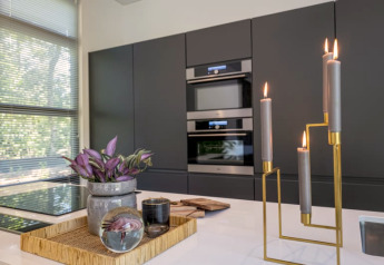 Moderne lodgekeuken met donkere kasten, grote ramen, decoratief dienblad en brandende kaarsen.