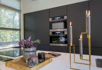 Cucina moderna di un lodge con armadi scuri, grandi finestre, vassoio decorativo e candele accese.