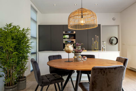 Modern lodge dining area with round wooden table, gray chairs, green plant, and bamboo pendant lamp.