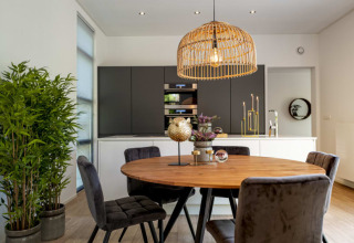 Moderne lodge spisestue med rundt træbord, grå stole, grøn plante og hængende bambuslampe.