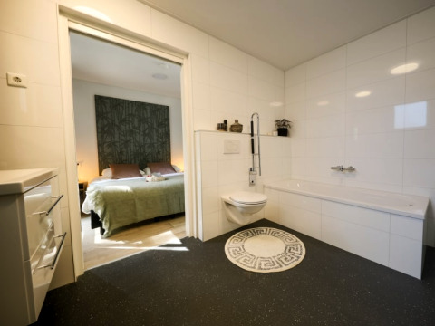 Salle de bain moderne avec toilettes murales et baignoire, donnant sur une chambre confortable en lodge.