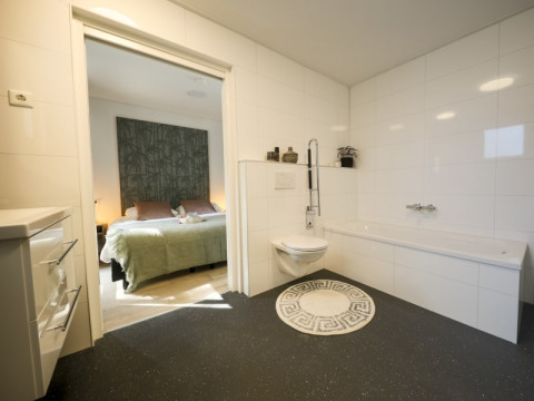 Salle de bain moderne avec toilettes murales et baignoire, donnant sur une chambre confortable en lodge.