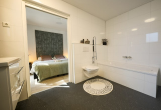 Baño moderno en un lodge con inodoro suspendido, alfombra redonda y acceso directo al dormitorio.