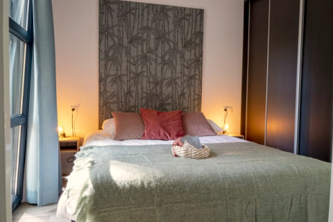 Chambre confortable d’un lodge avec grand lit, plaid vert, coussins roses et ambiance lumineuse douce.