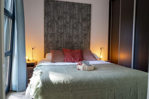 Dormitorio acogedor en una cabaña, con cama grande, manta verde, cojines rosas y luz ambiental suave.