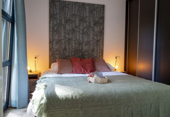Soveværelse med stor seng, grøn plaid, rosa puder og dæmpet belysning, fotograferet på et lodge.