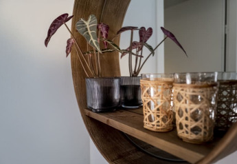 Decoración acogedora de lodge con planta en maceta y vasos forrados de mimbre sobre estante de madera.