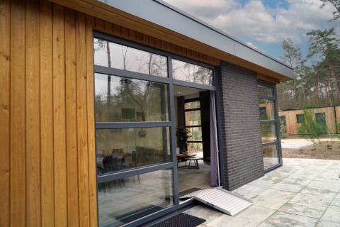 Photo extérieure d'un lodge moderne avec de grandes fenêtres, bardage bois et rampe d'accessibilité.