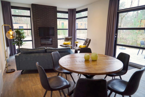 Salon moderne de lodge avec grandes fenêtres, table ronde en bois et vue confortable sur la forêt