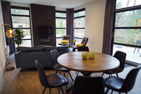 Modern lodge living room with large windows, round wooden dining table, and cozy forest views outside