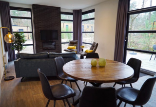 Salón moderno de una cabaña con grandes ventanales, mesa redonda de madera y vistas al bosque