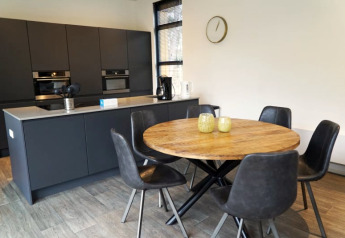 Moderne lodgekeuken met ronde houten tafel, vijf zwarte stoelen, donkere kasten en een wandklok.