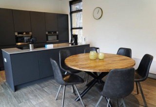 Cocina moderna en una cabaña con mesa redonda de madera, cinco sillas negras y armarios oscuros.
