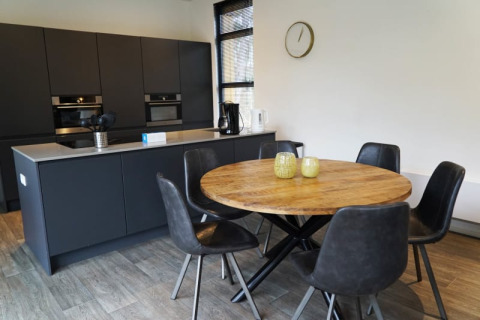 Cocina moderna en una cabaña con mesa redonda de madera, cinco sillas negras y armarios oscuros.
