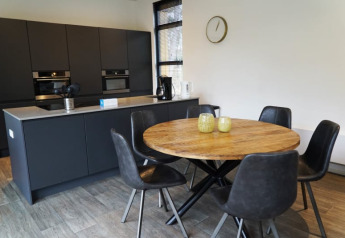 Cocina moderna en una cabaña con mesa redonda de madera, cinco sillas negras y armarios oscuros.
