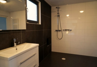 Salle de bain moderne dans un lodge, avec douche à l'italienne, murs carrelés et meuble blanc.
