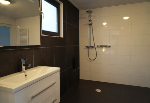 Baño moderno en un lodge con ducha a nivel de suelo, paredes de azulejos y lavabo blanco elegante.