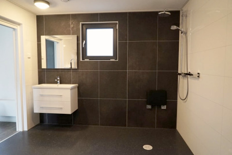 Salle de bain moderne dans un lodge avec vasque suspendue, carrelage foncé, fenêtre et douche.