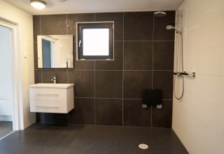 Salle de bain moderne dans un lodge avec vasque suspendue, carrelage foncé, fenêtre et douche.