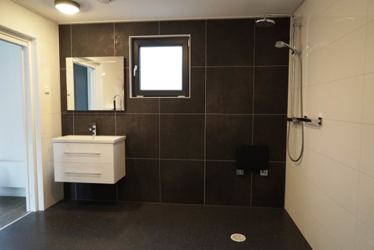 Baño moderno en una cabaña con lavabo flotante, azulejos oscuros, ventana y ducha tipo lluvia.