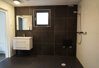 Baño moderno en una cabaña con lavabo flotante, azulejos oscuros, ventana y ducha tipo lluvia.