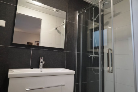 Salle de bain moderne dans un lodge avec grand miroir, lavabo blanc, douche en verre et carrelage foncé.