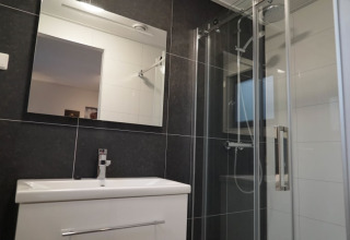 Modern lodge bathroom with large mirror, white sink, glass shower, and dark wall tiles.