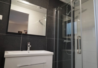 Salle de bain moderne dans un lodge avec grand miroir, lavabo blanc, douche en verre et carrelage foncé.