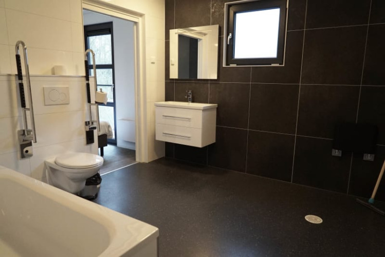 Baño accesible en una cabaña con sanitarios modernos, paredes de azulejo negro y ventana grande.