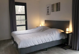 Chambre confortable dans un lodge avec deux lits simples, tables de nuit, lampes et vue extérieure.