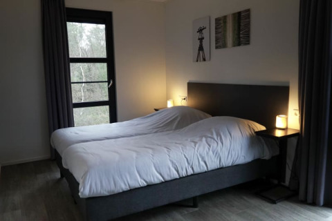 Chambre confortable dans un lodge avec deux lits simples, tables de nuit, lampes et vue extérieure.