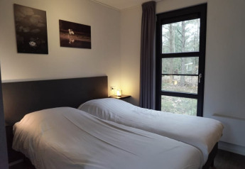 Et hyggeligt soveværelse i en lodge med to enkeltsenge, store vinduer og naturskøn udsigt til skov.
