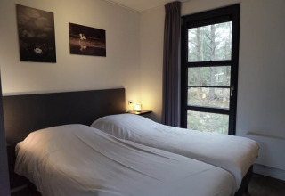 Et hyggeligt soveværelse i en lodge med to enkeltsenge, store vinduer og naturskøn udsigt til skov.