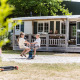 Børn leger udenfor en familiehytte, mens voksne sidder på verandaen i Kampeerdorp de Zandstuve, Holland.